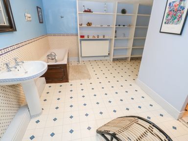 A bathroom with a sink, bathtub, built-in shelves, a wicker chair, and a framed picture at Eden House Edenhall near Penrith