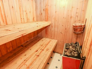 A wooden sauna room with two bench seats stones on a heater and a wooden bucket at Eden House Edenhall near Penrith