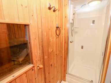 A shower with white tiles and a wooden sauna room with a glass window at Eden House in Edenhall near Penrith