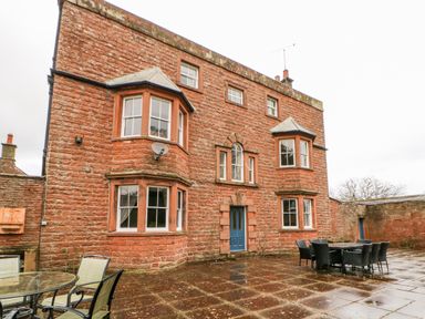 A brick building with blue door and multiple windows with outdoor tables and chairs on tiled patio at Eden House in Edenhall near Penrith