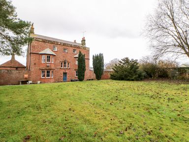 A red brick house with windows and a lawn in front of it with trees and bushes at Eden House Edenhall near Penrith