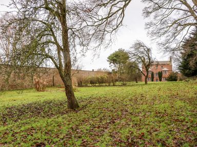 A grassy garden with scattered trees and a brick house in the background at Eden House in Edenhall near Penrith