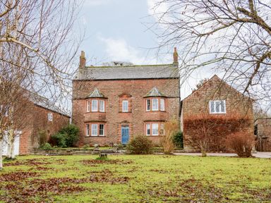 A front view of a brick house with a blue door and bay windows at Eden House Edenhall near Penrith