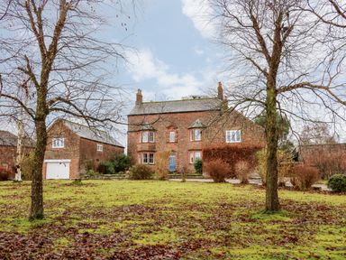 A brick two story house with a blue door and a detached garage in front of a grass yard with two leafless trees at Eden House Edenhall near Penrith