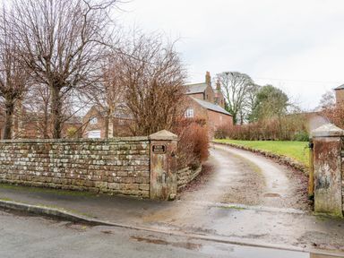A driveway lined with stone walls leading to a brick house with leafless trees at Eden House Edenhall near Penrith