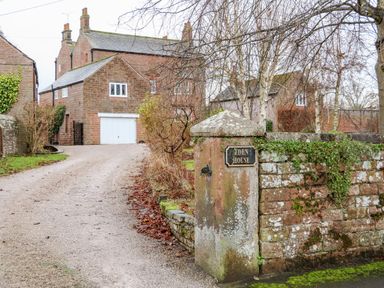 A stone driveway leading to a brick house with a white garage door and a stone wall with a sign reading Eden House at Eden House Edenhall near Penrith