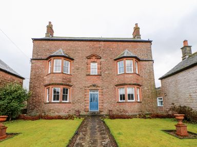 A front view of a brick house with a blue door and bay windows on both sides at Eden House in Edenhall near Penrith