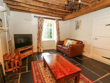 A living room with a leather sofa wooden coffee table television and floral curtains at Penuwch Fach in Aberystwyth