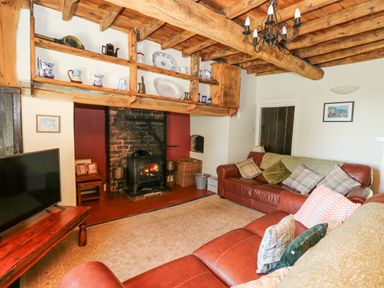 A living room with a wood burning stove wooden beams on the ceiling and leather sofas at Penuwch Fach in Aberystwyth