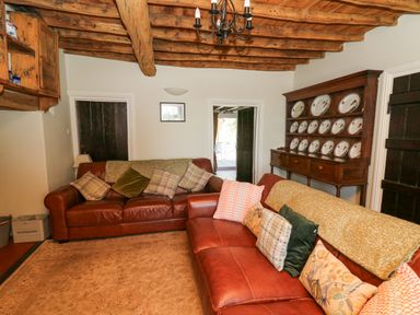 A living room with leather sofas cushions a wooden plate rack and exposed wooden beams on the ceiling at Penuwch Fach in Aberystwyth