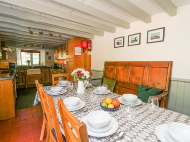 A dining area with a set table and wooden chairs next to a kitchen with wooden cabinets at Penuwch Fach in Aberystwyth