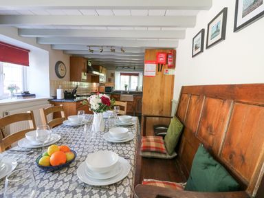 A dining area with a table set for six and a wooden bench with cushions by a kitchen at Penuwch Fach in Aberystwyth