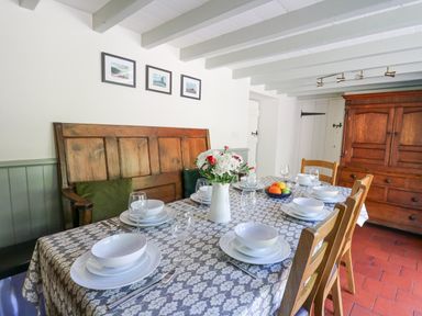 A dining room with a table set for six with white dishes a vase of flowers a bowl of fruit wooden chairs and a wooden bench at Penuwch Fach in Aberystwyth