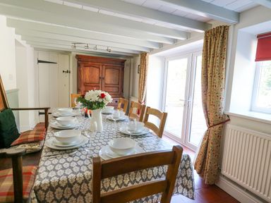 A dining room with a table set with plates bowls and glasses with a flower vase by doors at Penuwch Fach in Aberystwyth