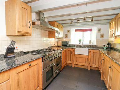 A kitchen with wooden cabinets a stainless steel stove a microwave and a sink under a window at Penuwch Fach in Aberystwyth
