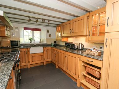 A kitchen with wooden cabinets granite countertops a white farm sink and various small appliances at Penuwch Fach in Aberystwyth