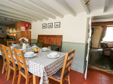 A dining room with a table set with plates glasses and flowers and wooden chairs with a doorway leading to a living room at Penuwch Fach in Aberystwyth