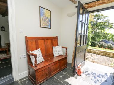 A wooden bench with cushions in a hallway next to a door open to a garden at Penuwch Fach in Aberystwyth