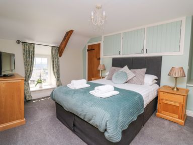 A bedroom with a double bed with pillows and towels two wooden bedside tables with lamps a dresser with a television a window with curtains and exposed wooden beam at Penuwch Fach in Aberystwyth