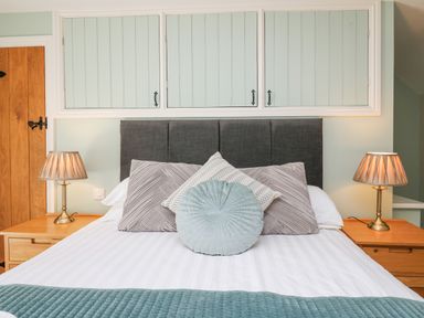 A bedroom with a bed with multiple pillows two bedside tables with lamps and built in cabinets above the bed at Penuwch Fach in Aberystwyth