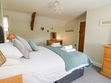 A bedroom with a bed, pillows, folded towels, wooden furniture, heart wall decorations and a wooden door at Penuwch Fach in Aberystwyth