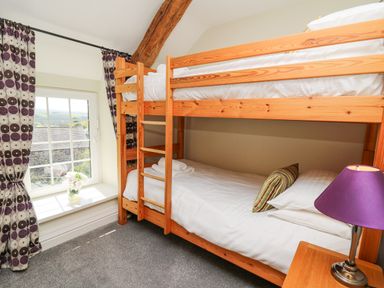 A bedroom with wooden bunk beds a window with patterned curtains and a lamp on a wooden bedside table at Penuwch Fach in Aberystwyth
