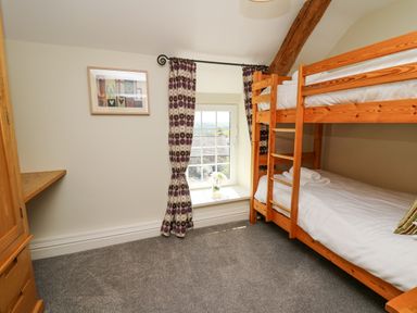 A bedroom with wooden bunk beds a window with patterned curtains and a framed picture on the wall at Penuwch Fach in Aberystwyth