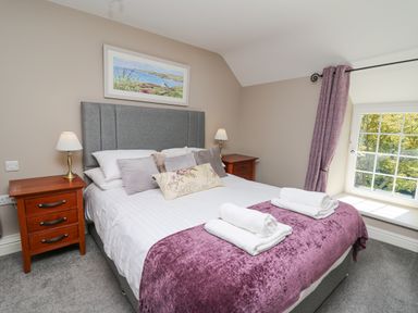 A bedroom with a double bed two bedside tables with lamps and a window with purple curtains at Penuwch Fach in Aberystwyth
