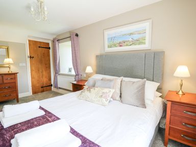 A bedroom with a bed with pillows and towels a wooden door a chest of drawers with a lamp and a framed picture on the wall at Penuwch Fach in Aberystwyth