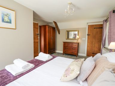 A bedroom with a bed with pillows and folded towels a wooden wardrobe a wooden dresser with a lamp and mirror and wooden doors at Penuwch Fach in Aberystwyth