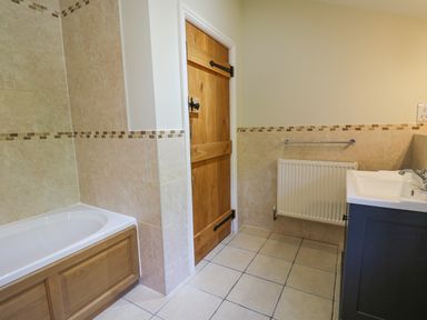 A bathroom with a bathtub a wooden door a radiator and a sink at Penuwch Fach in Aberystwyth