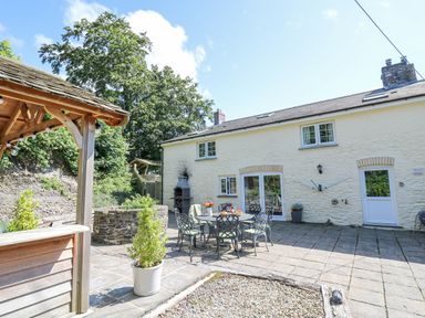 An outdoor patio area with metal chairs and table a wooden gazebo and potted plants at Penuwch Fach in Aberystwyth