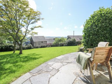 A garden with grass lawn and trees next to wooden chairs on a stone patio at Penuwch Fach in Aberystwyth