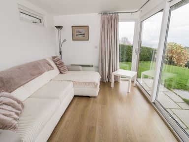A sitting area with a sectional sofa and a small white table by a glass sliding door at Bron Heulog Cottage in Llangoed near Beaumaris