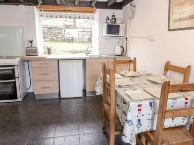 A kitchen with dining table set for four with glasses and plates at Bron Heulog Cottage in Llangoed near Beaumaris