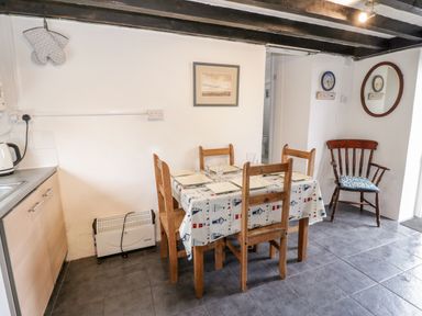 A dining area with a wooden table and chairs set for four with a patterned tablecloth and a wooden armchair with a cushion at Bron Heulog Cottage Llangoed near Beaumaris