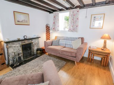 A living room with stone fireplace two sofas wooden side tables and floral curtains at Bron Heulog Cottage in Llangoed near Beaumaris