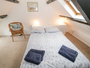A bedroom with a double bed with patterned bedding two folded towels a wicker chair and a skylight window at Bron Heulog Cottage in Llangoed near Beaumaris
