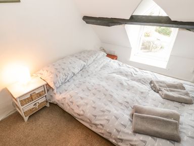 A bedroom with a bed with grey patterned bedding folded towels on the bed a window on the slanted ceiling and a bedside table with a lamp at Bron Heulog Cottage Llangoed near Beaumaris