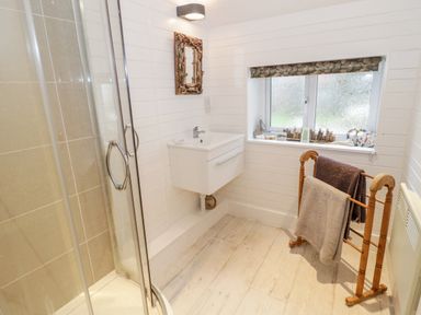 A bathroom with a glass shower enclosure a small white sink a wooden towel rack and a window with decorations on the sill at Bron Heulog Cottage in Llangoed near Beaumaris