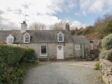 A stone cottage with a gravel driveway and potted plants at Bron Heulog Cottage Llangoed near Beaumaris