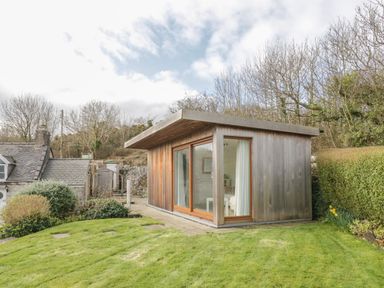 A small wooden garden room with glass sliding doors on a grassy lawn near trees and bushes at Bron Heulog Cottage Llangoed near Beaumaris