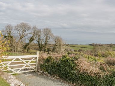A wooden gate opening to a gravel path with trees and fields in the background at Bron Heulog Cottage Llangoed near Beaumaris