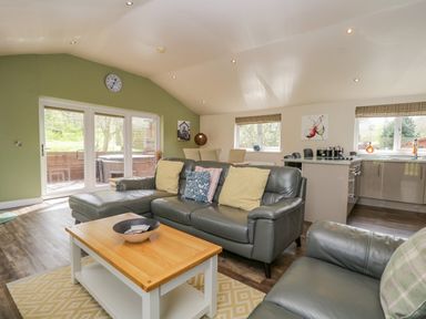 A living room with grey leather sofas and a wooden coffee table next to a dining area and kitchen at Cartmel Lodge in Allithwaite near Grange-over-Sands