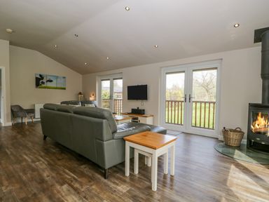 A living room with a sofa and armchair a wood burning stove and double doors opening to a garden at Cartmel Lodge in Allithwaite near Grange-over-Sands