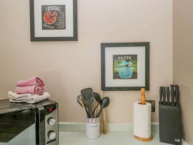 A kitchen counter with a microwave oven with towels on top a container with cooking utensils paper towel holder and a knife block on the countertop at Cartmel Lodge in Allithwaite near Grange-over-Sands