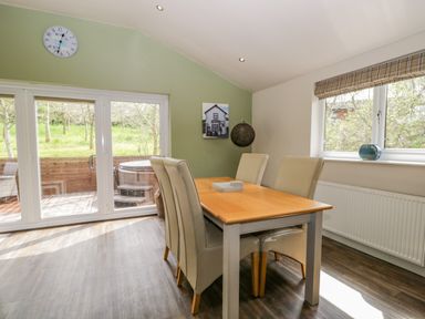 A dining area with a wooden table and four beige chairs next to sliding glass doors and a window at Cartmel Lodge in Allithwaite near Grange-over-Sands