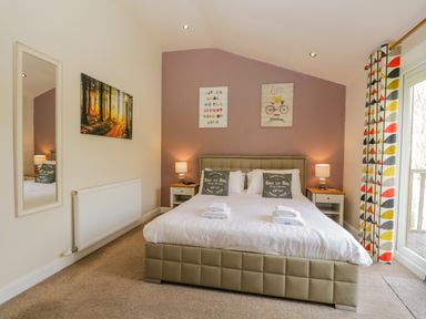 A bedroom with a double bed with white bedding two bedside tables with lamps a wall mirror and patterned curtains at Cartmel Lodge in Allithwaite near Grange-over-Sands