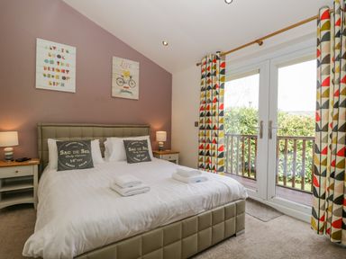 A bedroom with a bed and two bedside tables with lamps and patterned curtains at Cartmel Lodge in Allithwaite near Grange-over-Sands