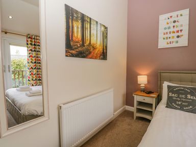 A bedroom with a bed pillow lamp bedside table mirror and wall art at Cartmel Lodge in Allithwaite near Grange-over-Sands